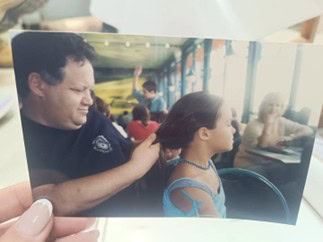 גבר מחזיק בעדינות את שיערה של ילדה קטנה בזמן שהוא יושב ליד שולחן בחדר הומה אדם, כשברקע נראים אנשים נוספים. - דפנה פורמן, הרצאות, ייעוץ וטיפול רגשי במעברים וברילוקיישןש