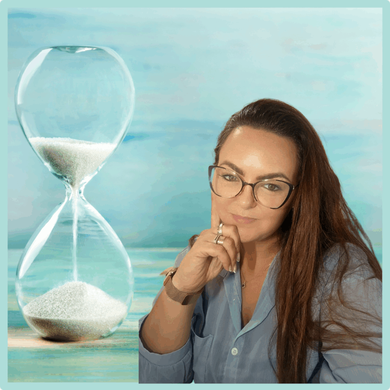 אישה עם שיער חום ארוך ומשקפיים יושבת מהורהרת ליד שעון חול גדול עם חול לבן על רקע כחול רך. - דפנה פורמן, הרצאות, ייעוץ וטיפול רגשי במעברים וברילוקיישןש