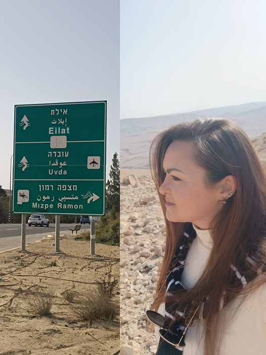 אישה עומדת בנוף סלעי ליד שלט דרכים המפנה לאילת, אובדה ומצפה רמון בישראל. - דפנה פורמן, הרצאות, ייעוץ וטיפול רגשי במעברים וברילוקיישןש