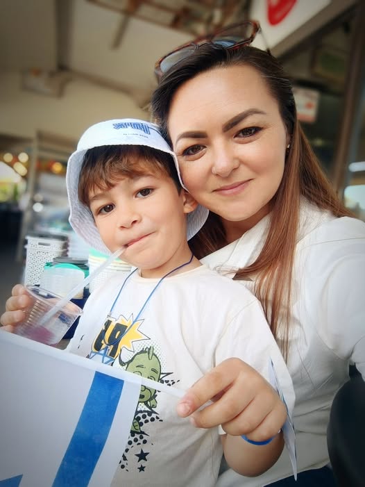 אישה וילד קטן יושבים יחד; הילד מחזיק משקה עם קשית ודגל ישראל. שניהם מביטים למצלמה ומחייכים. - דפנה פורמן, הרצאות, ייעוץ וטיפול רגשי במעברים וברילוקיישןש